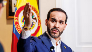 Colombian government official speaking at a press event with national flag in the background.