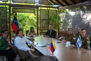 Goverment officials sitting around a long table in a conference room with plants in the background and flags of Venezuela and Israel set in front of them.