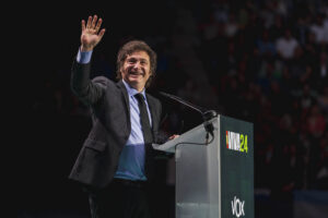 Javier Milei, Argentinian President, standing in front of a podium with his hand raised in a wave.