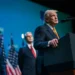 President Donald Trump speaks at a podium during a public event with US officials standing behind him.
